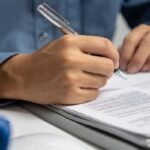 Pessoa escrevendo num livro sobre uma mesa